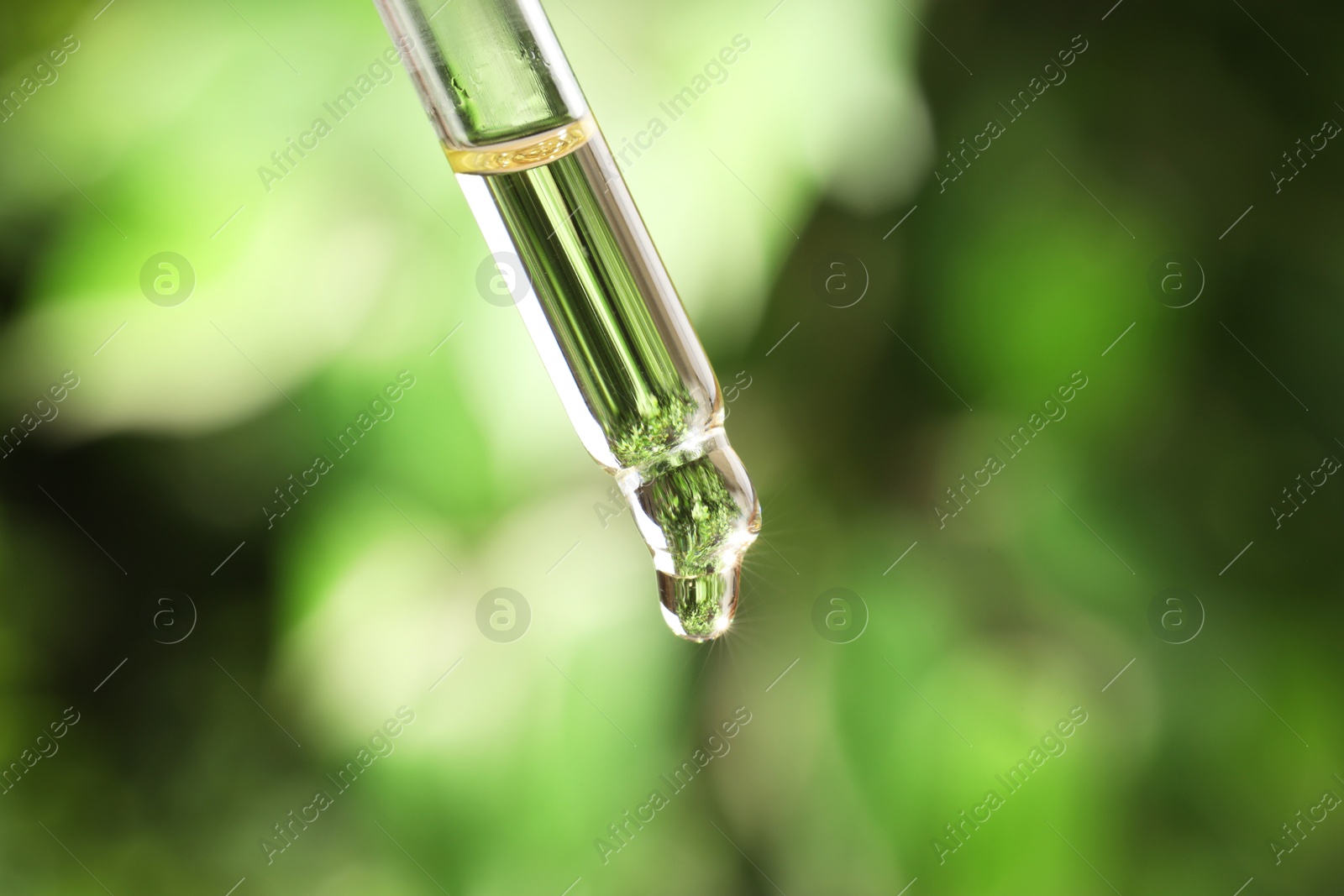 Photo of Essential oil dripping from pipette against blurred green background, closeup