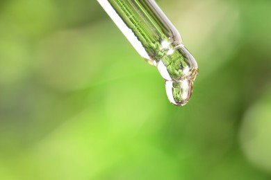 Photo of Essential oil dripping from pipette against blurred green background, closeup. Space for text