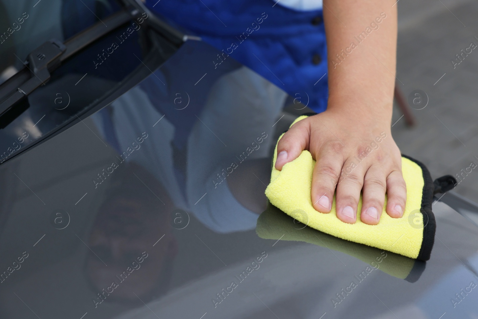 Photo of Man wiping car hood with yellow rag, closeup