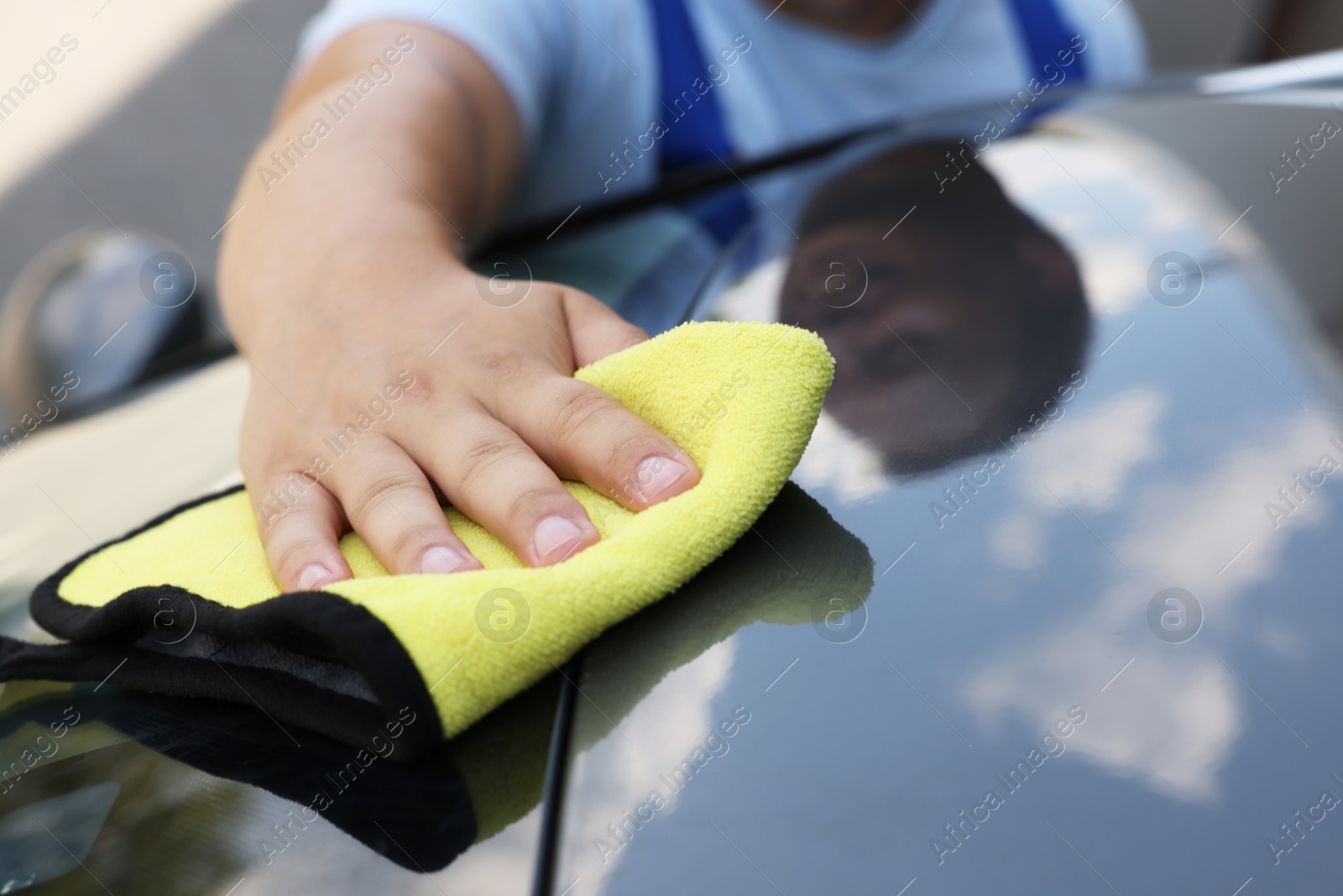 Photo of Man wiping car hood with yellow rag, closeup