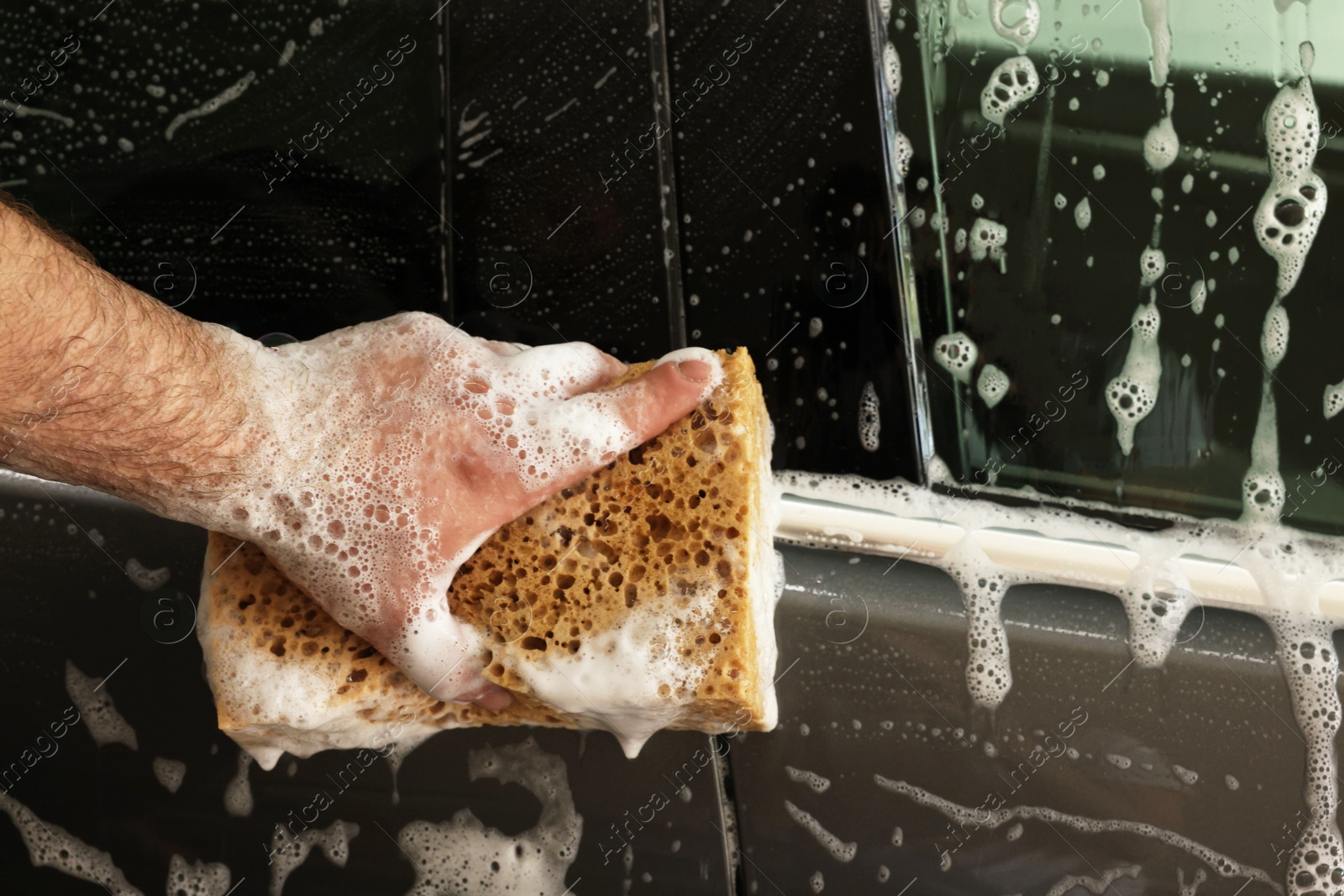 Photo of Man washing auto with sponge at car wash, closeup