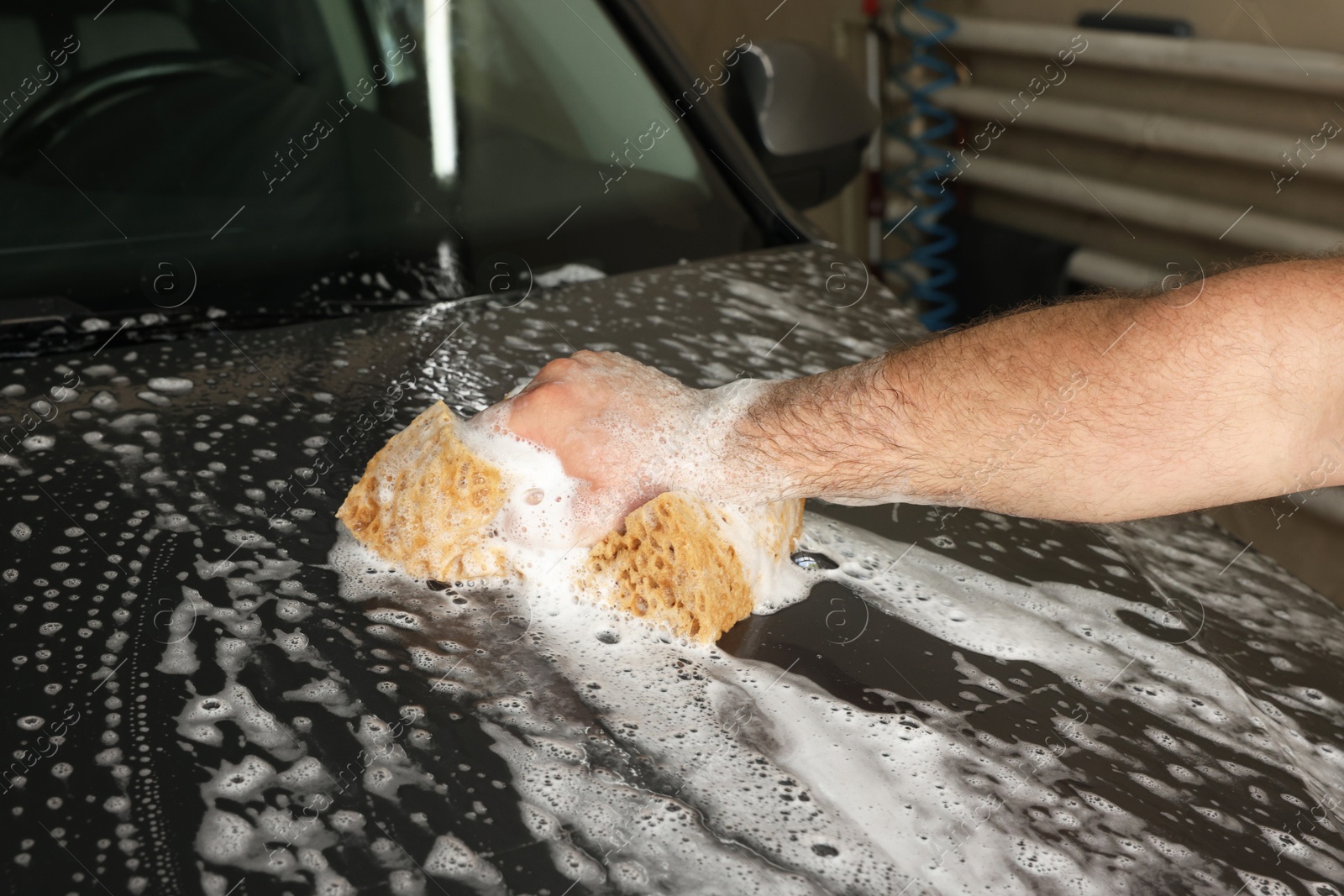 Photo of Man washing car hood with sponge indoors, closeup