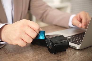 Photo of Man making payment via terminal while using laptop at wooden table, closeup