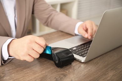 Photo of Man making payment via terminal while using laptop at wooden table, closeup