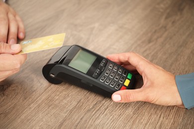 Photo of Woman taking payment from client via credit card terminal at wooden table, closeup