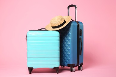 Photo of Two new color suitcases and wicker hat on pink background