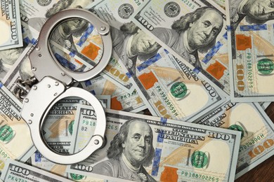 Photo of Handcuffs on pile of dollar banknotes, flat lay. Space for text