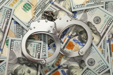 Photo of Handcuffs on pile of dollar banknotes, flat lay