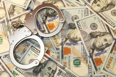 Handcuffs on pile of dollar banknotes, flat lay. Space for text