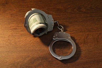 Photo of Handcuffs with dollar banknotes on wooden table