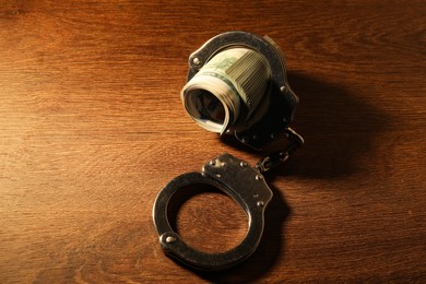 Handcuffs with dollar banknotes on wooden table