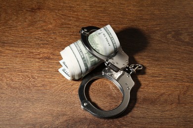 Photo of Handcuffs with dollar banknotes on wooden table