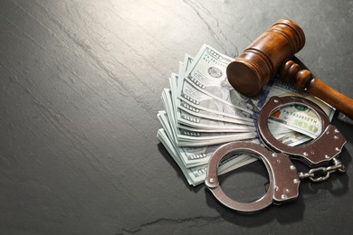 Handcuffs with dollar banknotes and wooden gavel on grey textured table. Space for text