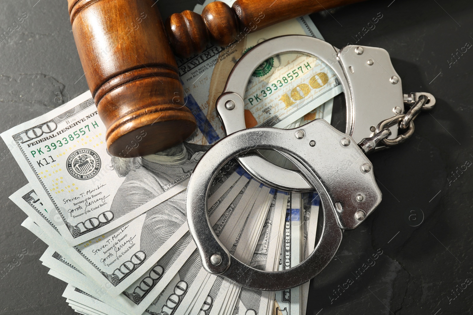 Photo of Handcuffs with dollar banknotes and wooden gavel on grey textured table, flat lay