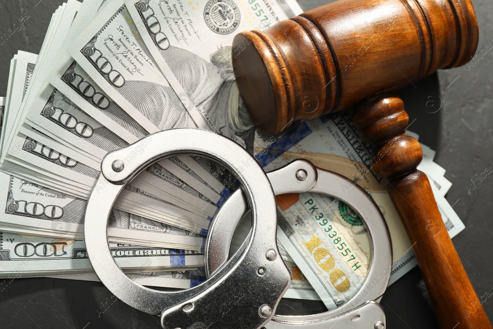 Photo of Handcuffs with dollar banknotes and wooden gavel on grey textured table, flat lay