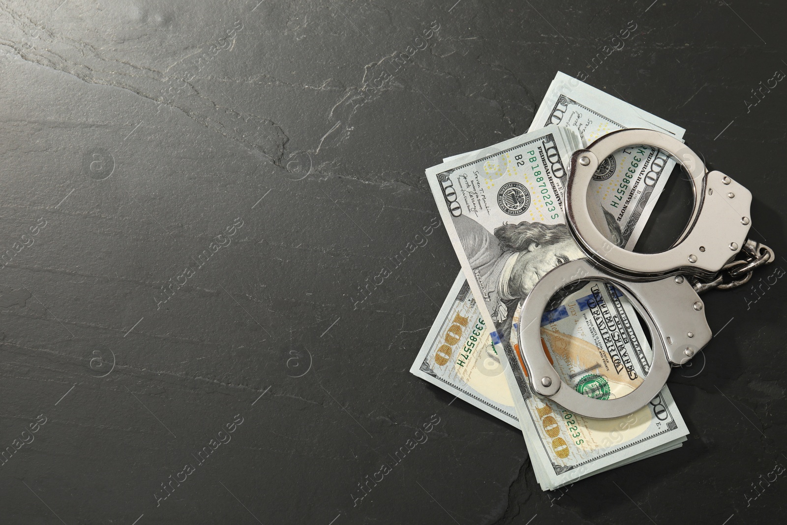 Photo of Handcuffs with dollar banknotes on grey textured table, flat lay. Space for text