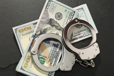 Photo of Handcuffs with dollar banknotes on grey textured table, flat lay