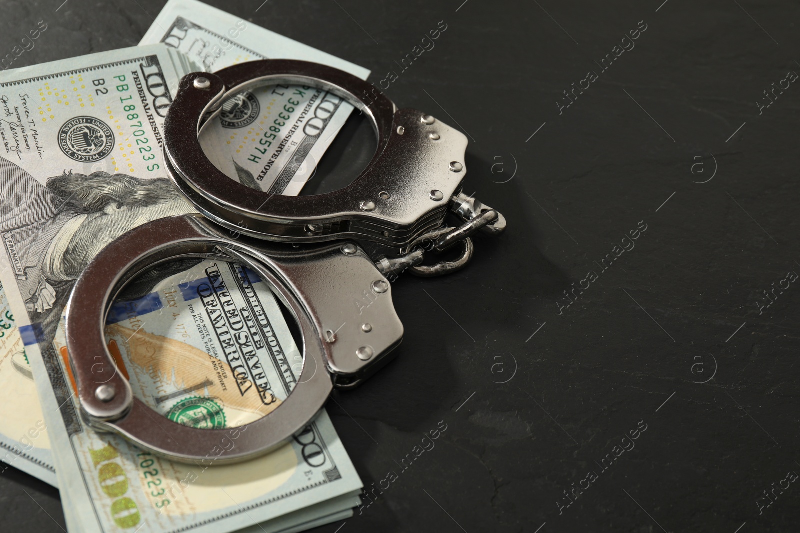 Photo of Handcuffs with dollar banknotes on grey textured table, space for text