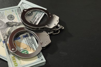 Handcuffs with dollar banknotes on grey textured table, space for text