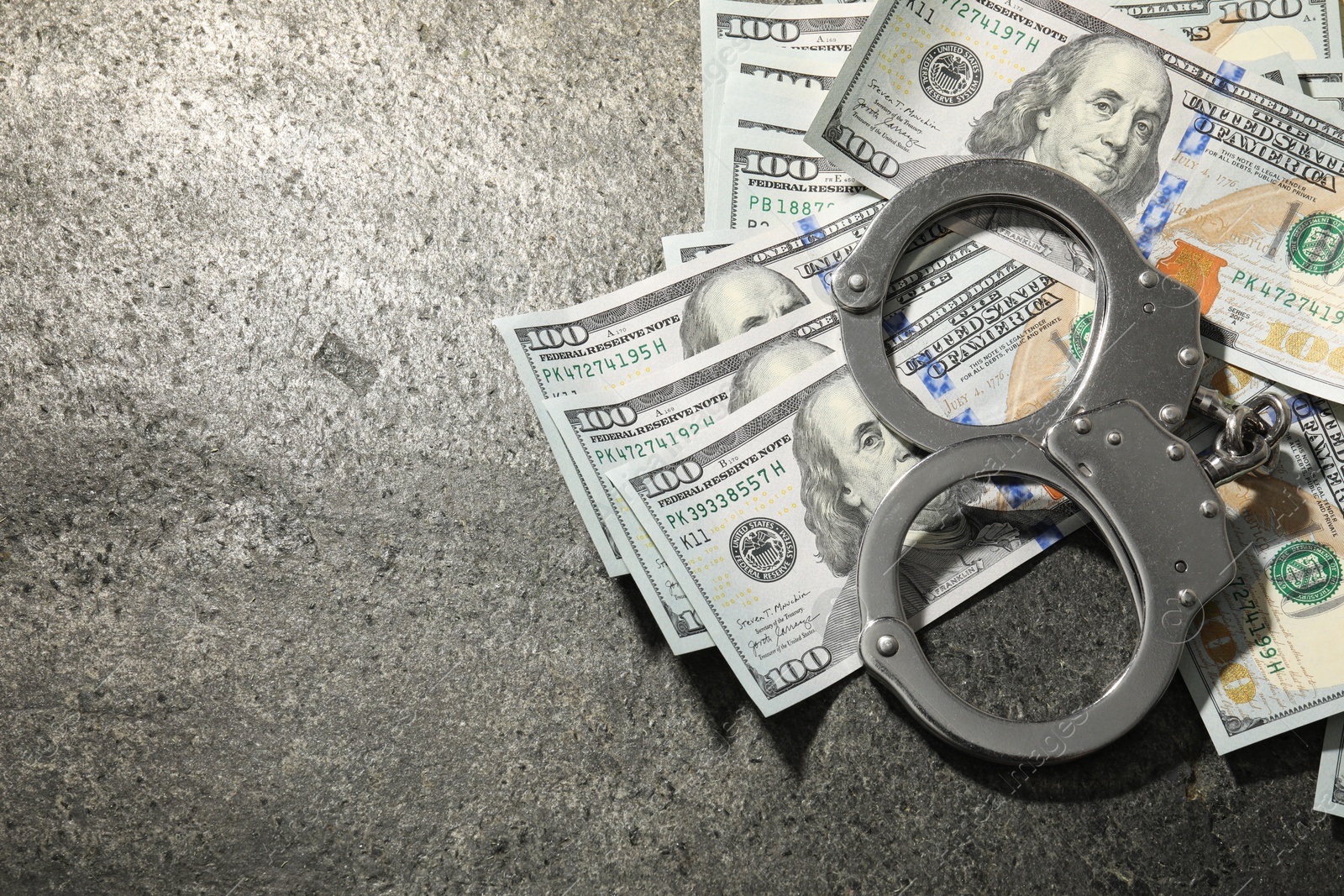 Photo of Handcuffs with dollar banknotes on grey textured table, flat lay. Space for text