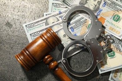 Handcuffs with dollar banknotes and wooden gavel on grey textured table, flat lay