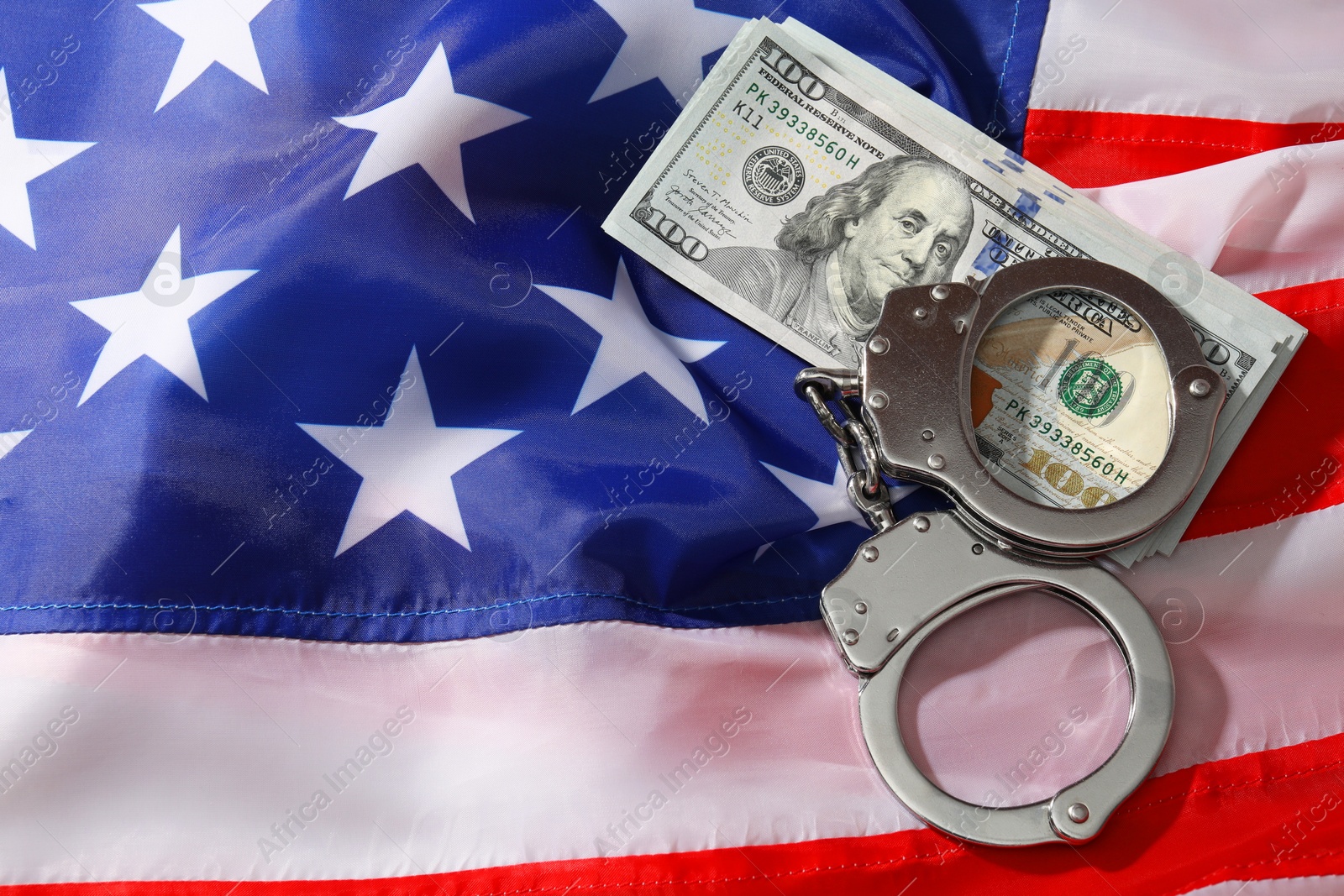 Photo of Handcuffs with dollar banknotes on American flag, flat lay. Space for text