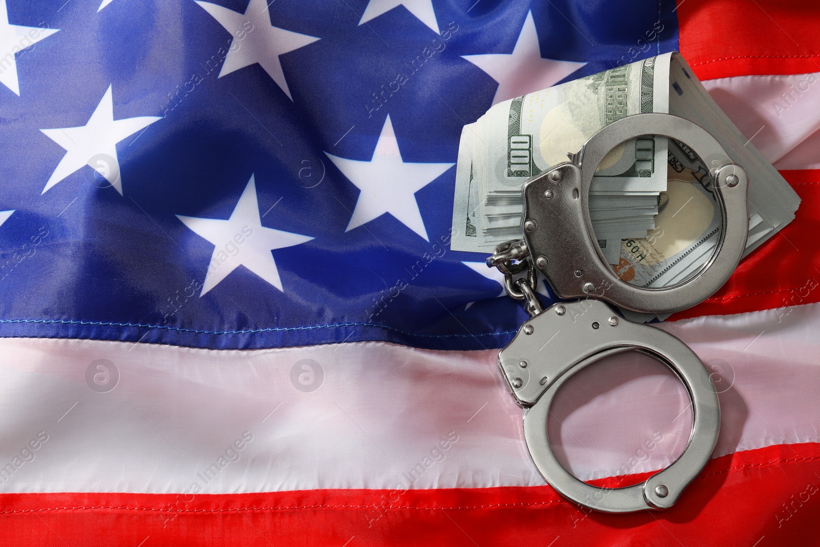 Photo of Handcuffs with dollar banknotes on American flag, flat lay. Space for text