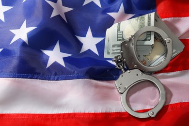 Handcuffs with dollar banknotes on American flag, flat lay. Space for text