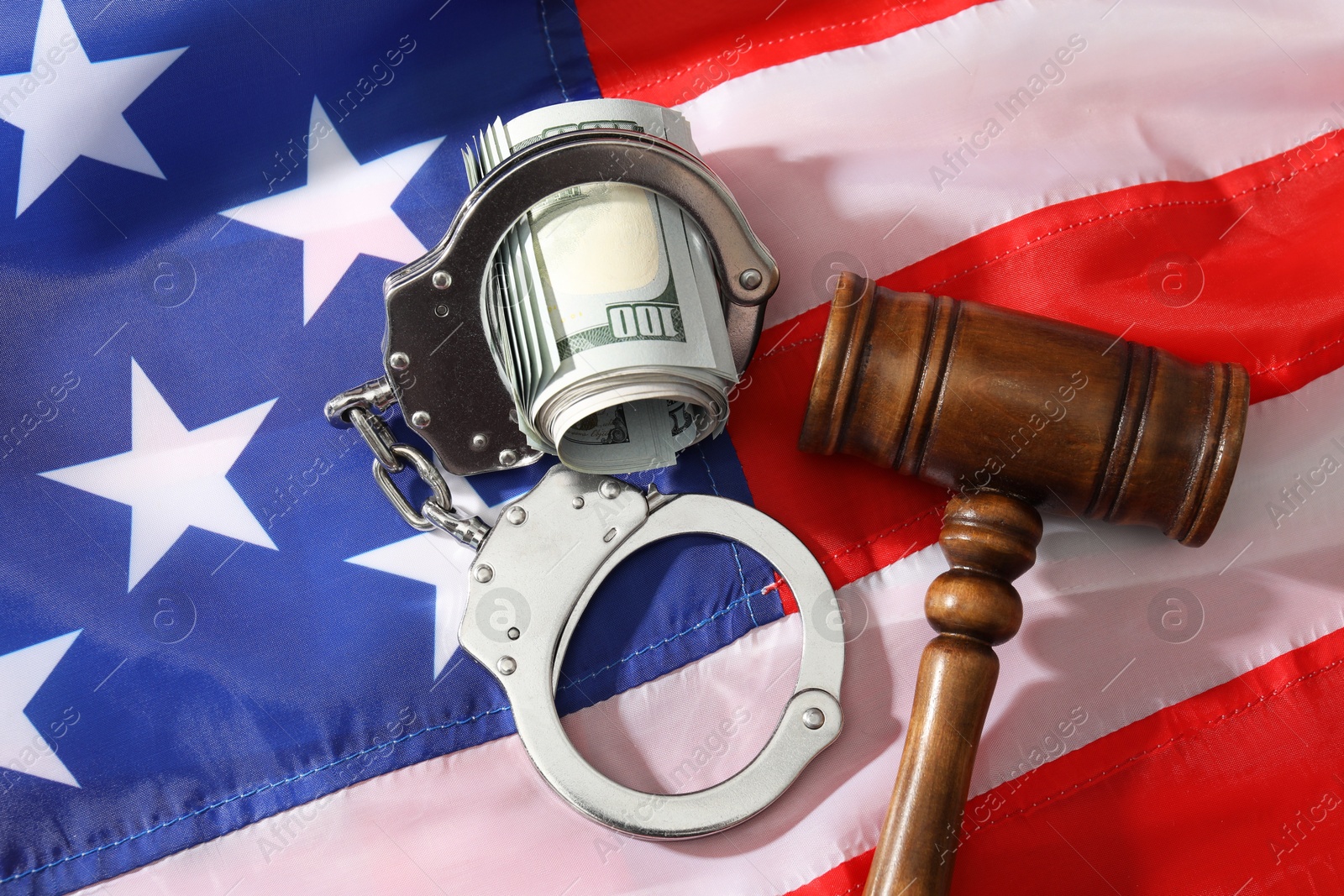 Photo of Handcuffs with dollar banknotes and wooden gavel on American flag, flat lay