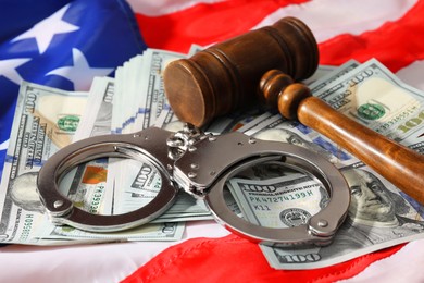 Handcuffs with dollar banknotes and wooden gavel on American flag