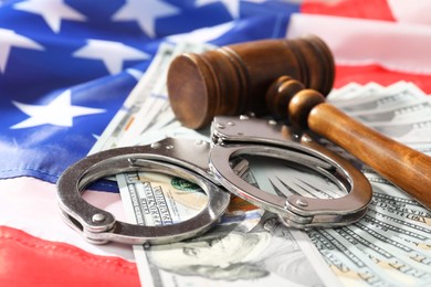 Photo of Handcuffs with dollar banknotes and wooden gavel on American flag, closeup