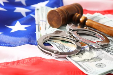 Handcuffs with dollar banknotes and wooden gavel on American flag