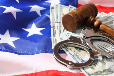 Handcuffs with dollar banknotes and wooden gavel on American flag