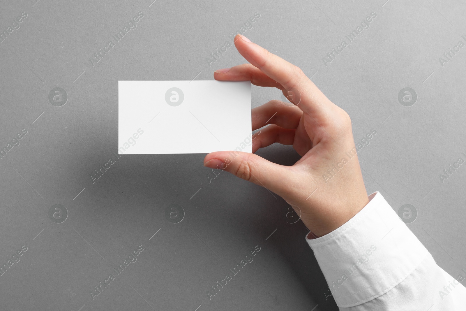 Photo of Woman with blank business card on grey background, closeup. Mockup for design