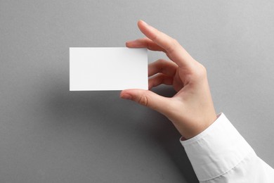 Woman with blank business card on grey background, closeup. Mockup for design