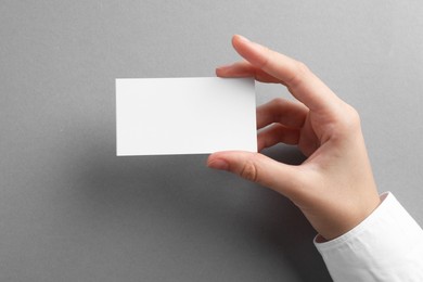 Woman with blank business card on grey background, closeup. Mockup for design