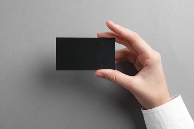 Woman with blank business card on grey background, closeup. Mockup for design