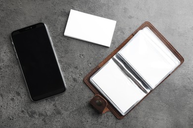 Photo of Leather card holder with blank business cards and smartphone on grey textured table, flat lay. Mockup for design