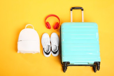 Photo of Turquoise suitcase with backpack, sneakers and headphones on yellow background, above view