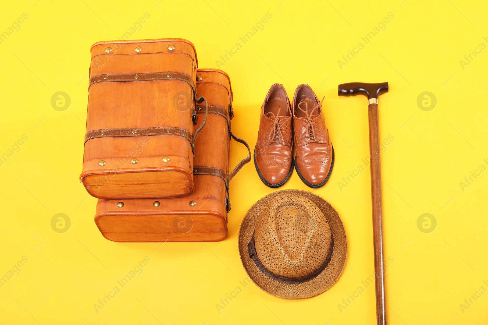 Photo of Suitcases, shoes, hat and cane on yellow background, above view