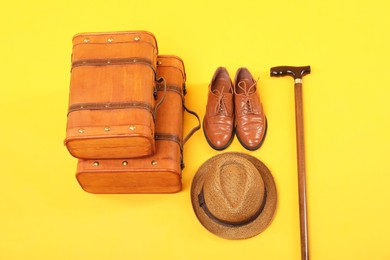 Photo of Suitcases, shoes, hat and cane on yellow background, above view