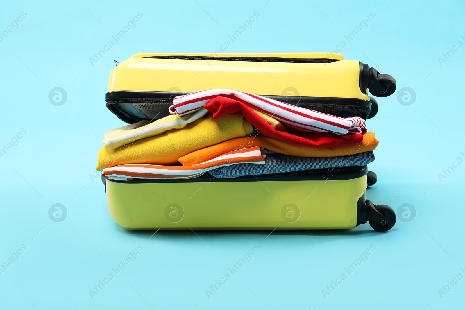 Photo of One suitcase with clothes on light blue background