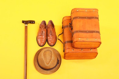 Photo of Suitcases, shoes, hat and cane on yellow background, above view