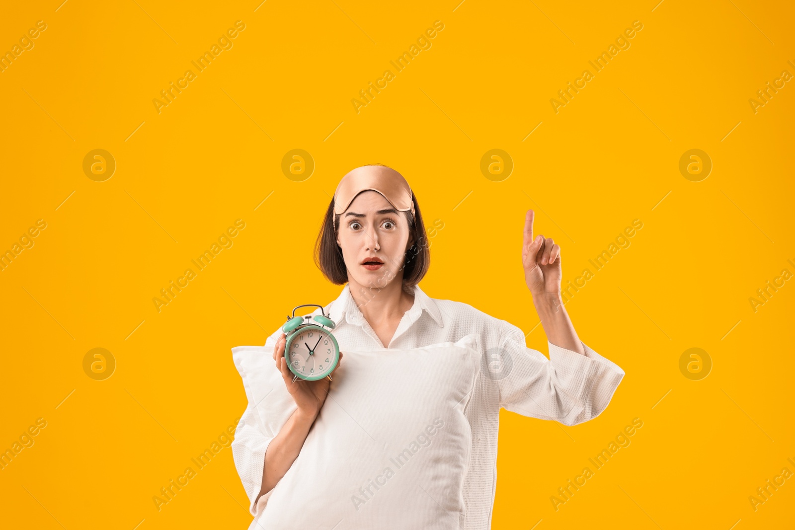 Photo of Overslept young woman with sleep mask, pillow and alarm clock on yellow background