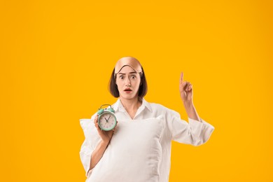 Photo of Overslept young woman with sleep mask, pillow and alarm clock on yellow background