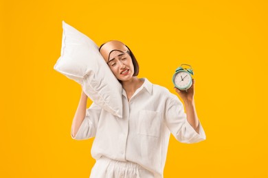 Photo of Overslept young woman with sleep mask, pillow and alarm clock on yellow background