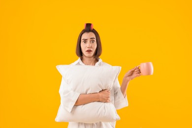 Photo of Overslept young woman with pillow and cup on yellow background