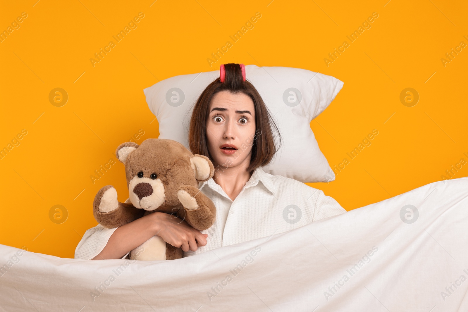 Photo of Overslept young woman with teddy bear, pillow and blanket on yellow background