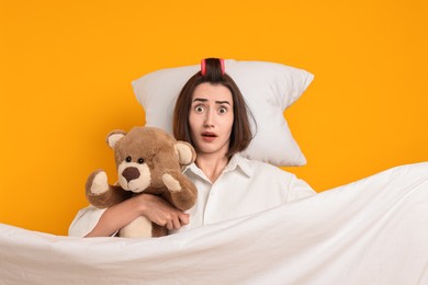 Overslept young woman with teddy bear, pillow and blanket on yellow background