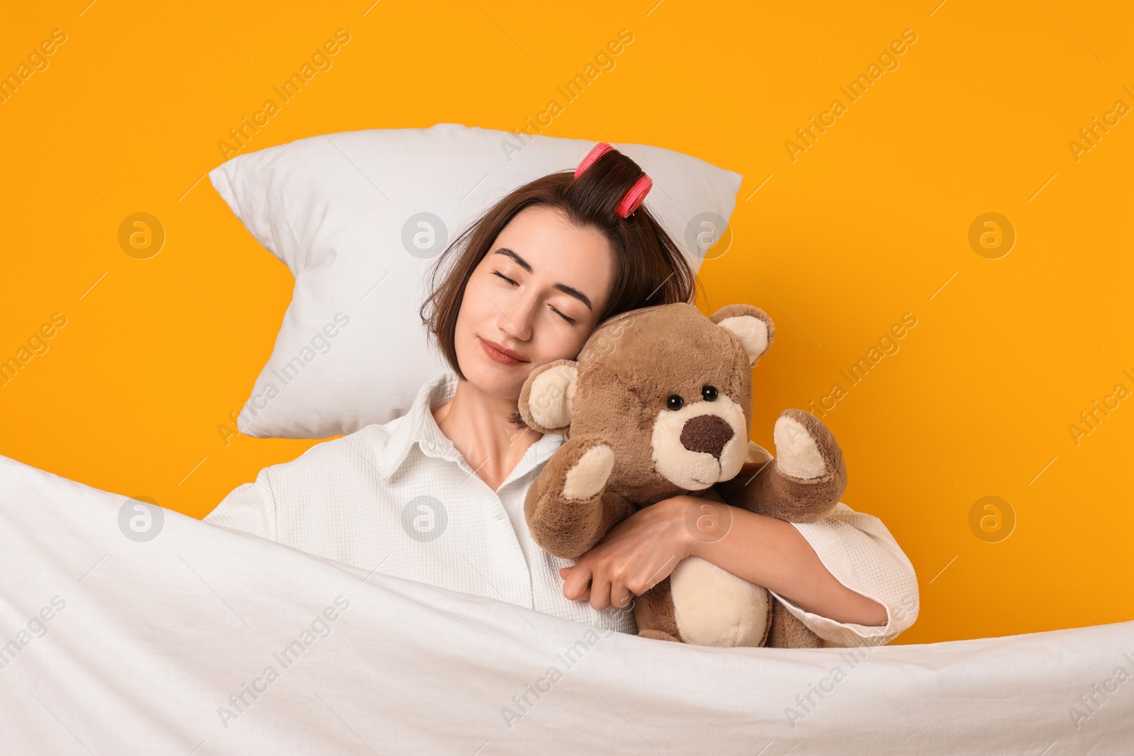 Photo of Overslept young woman with teddy bear, pillow and blanket on yellow background